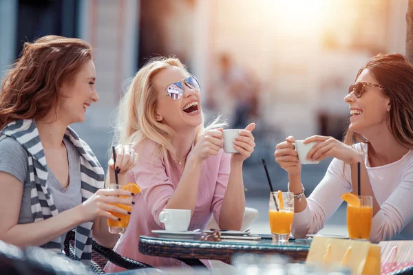 Three young women meeting at outdoor cafe and enjoying together.