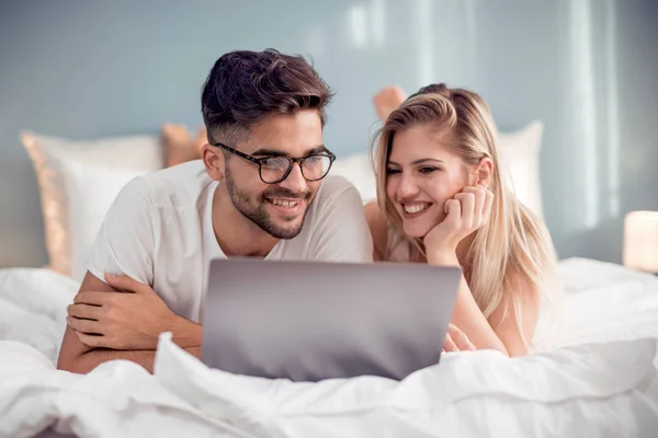 Young couple with laptop on bed.Man and woman enjoying watching video on laptop while relaxing in bedroom.