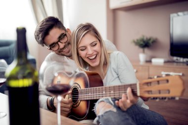 Genç güzel evde istirahat ve gitar çalmak çift. Yakışıklı erkek arkadaşı için gitar çalmak.