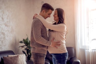 Yakışıklı ve güzel hamile eşi sarılma ve onların oturma odasında dururken gülümseyen.