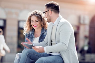 Açık havada eğleniyor ve gülümseyerek, tablet üzerinde seyir mutlu genç Çift.