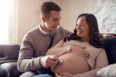 Mutluluk koca stetoskop sınav yatakta hamile eşi karnına için kullanıyor.