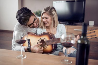 Genç ve güzel bir çift evde dinleniyor ve gitar çalıyor..