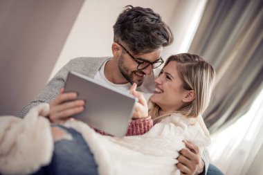 Şirin çift altında battaniye evde oturma odasında kanepede rahatlatıcı ve tablet kullanma.