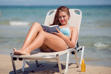 genç kadın bir plajda denize yakın bir kitapla rahatlatıcı.