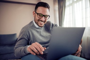 Genç adam koltukta ev ofis, laptop ile çalışma.