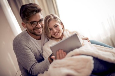 Şirin çift altında battaniye evde oturma odasında kanepede rahatlatıcı ve tablet kullanma.