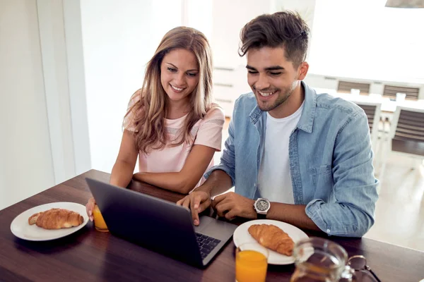 People, communication, technology,food and drink.Young couple having breakfast while looking something on laptop.
