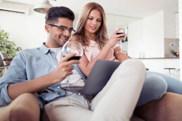 居間でノート パソコンを見て赤ワインのグラスと美しい若いカップル — ストック写真