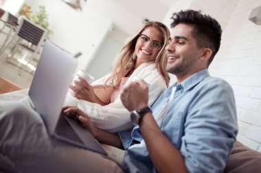 seven genç çift evde kanepede dizüstü kullanarak Kahve kupaları ile rahat.
