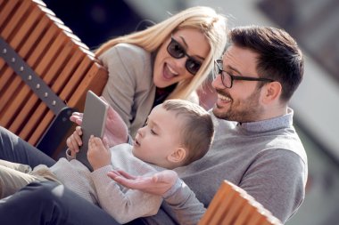 Mutlu bir aile ve dijital teknoloji. Anne ve küçük çocuk şehir parkta otururken tablet kullanma.