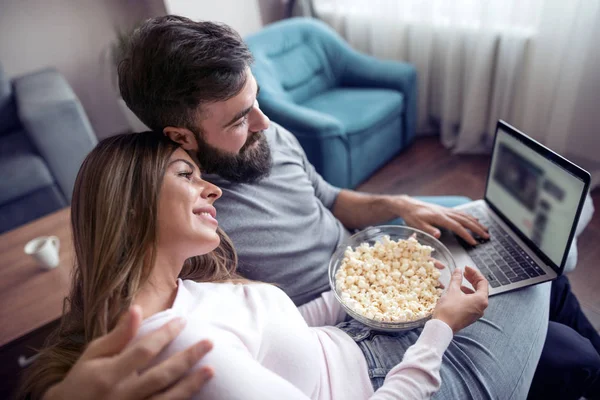 Dizüstü bilgisayar film izlerken patlamış mısır ile evde kanepede oturan mutlu genç çift.