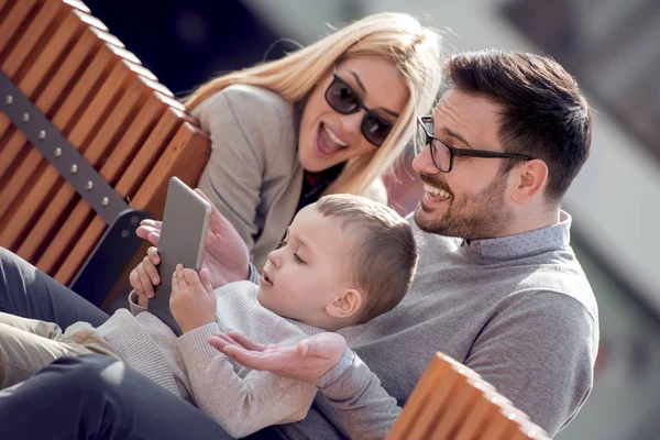 Happy family and digital technology. Young parents and little kid using tablet while sitting in the city park.