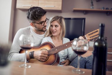 Genç ve güzel bir çift evde dinleniyor ve gitar çalıyor.