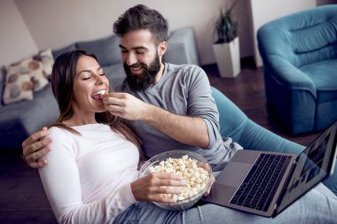 Dizüstü bilgisayar film izlerken patlamış mısır ile evde kanepede oturan mutlu genç çift.