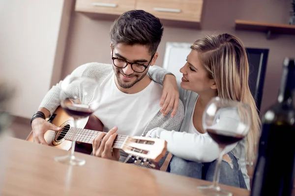 Genç ve güzel bir çift evde dinleniyor ve gitar çalıyor.