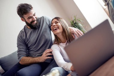 Oturma odası online alışveriş için dizüstü bilgisayar kullanarak bir kanepede oturan genç mutlu çift.