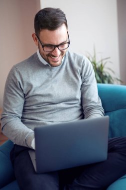 Genç adam, evde koltuk üstünde laptop ile çalışma office.