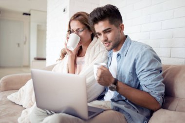 Evde kanepede dizüstü kullanarak kahve fincanı ile mutlu genç çift.