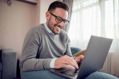 Genç adam, evde koltuk üstünde laptop ile çalışma office.