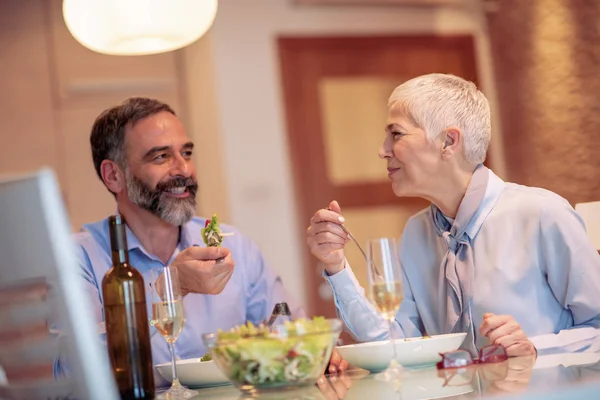 Mature couple toasting with wine while having lunch at their home.