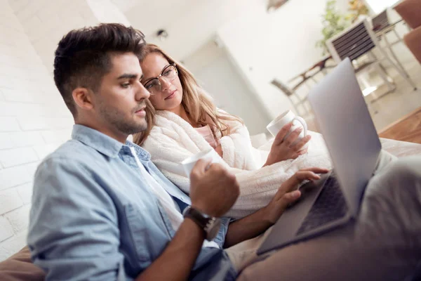 在家沙发上使用笔记本电脑的快乐的年轻夫妇与咖啡杯 — 图库照片