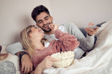 Mutlu genç çift kanepede evde patlamış mısır ile yalan ve Tv izlerken.