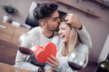 Güzel genç çift evde kutluyor. Yakışıklı adam kız arkadaşı bir hediye kutusu veriyor.