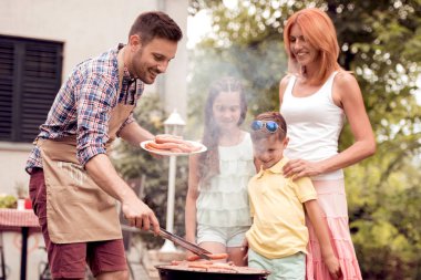 Adam aile kendi arka bahçesinde barbekü hazırlanıyor.