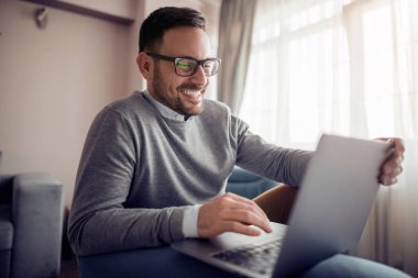 Genç adam, evde koltuk üstünde laptop ile çalışma office.