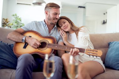 Aşık genç adam gitar çalmak süre kanepede oturan genç çift.
