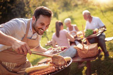 Yaz aylarında eğlenceli. Adam evin arka bahçesinde yaz aile öğle yemeği için et mangal üzerinde pişirme.