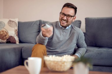 Süre evde bir kanepede oturan ve Tv izlerken mutlu genç adam yeme patlamış mısır portresi.