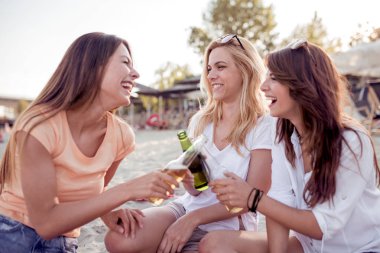 Grup Genç kadın arkadaşıyla kumsalda oturuyor ve içki ile kızartma.