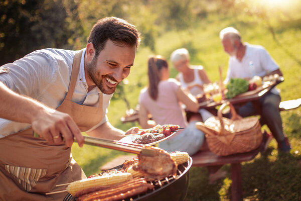 Летнее веселье. Человек готовит мясо на барбекю на летний семейный обед во дворе дома.
.