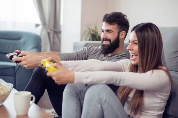 Happy couple sitting together in their living room and laughing while playing a video games.