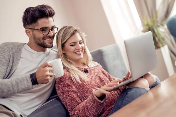 年轻的夫妇在他们的客厅里喝茶的同时使用一台笔记本电脑 — 图库照片
