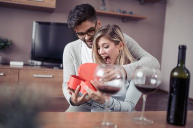 Güzel genç çift evde kutluyor. Yakışıklı adam kız arkadaşı bir hediye kutusu veriyor.