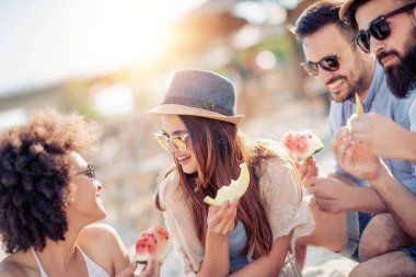 Sahilde eğleniyor ve karpuz yeme mutlu genç arkadaşlar.