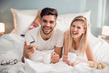Gülümseyen çift yatakta yatarken ve sabah evde kahve içme sırasında TV izlerken.