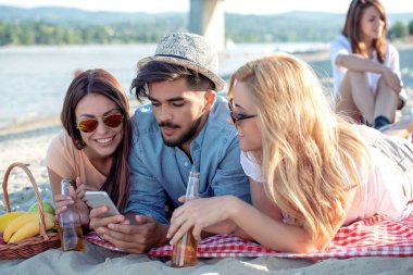 Bir adam ve iki kadın sahilde yalan, onlar telefonla arıyor ve gülümseyen.