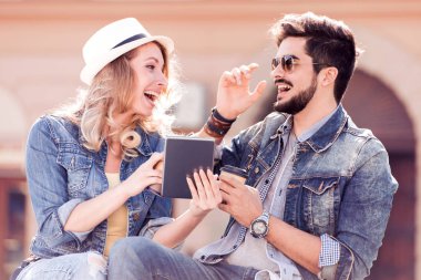 İki tablete arayan genç insanlar gülümsüyor. Portre tablet kentsel arka plan ve kahve ile çekici çift.