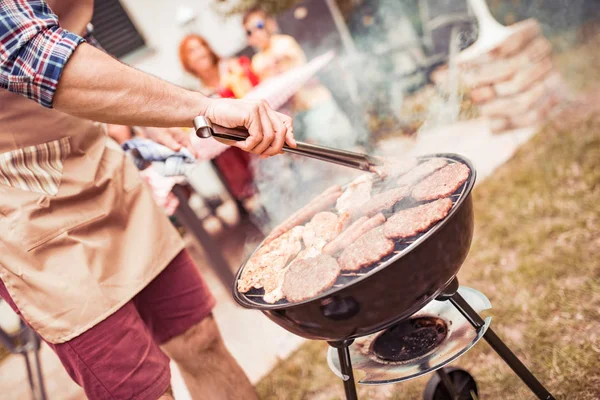 Man cooking meat on barbecue grill for his family at summer outdoor party,close up.