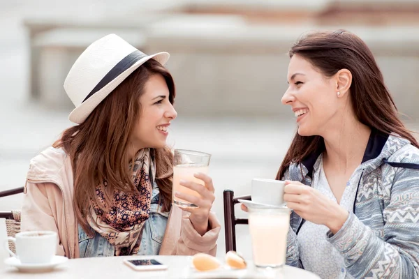 Two beautiful women having conversation, drinking coffee, lemonade and sitting in cafe.