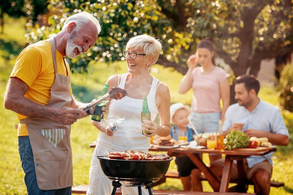 Happy big family gathered around the grill at picnic.Leisure,food,family and holidays concept.