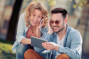 Tablet kullanma ve müzik açık havada için dinleme genç çift portresi.
