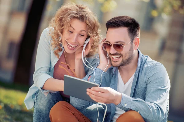 Tablet kullanma ve müzik açık havada için dinleme genç çift portresi.