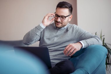 Genç adam, evde koltuk üstünde laptop ile çalışma office.