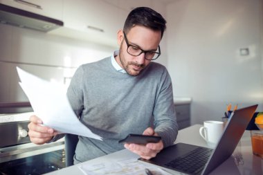 Mutfakta, oturma ve dizüstü bilgisayarda çalışma neşeli yakışıklı genç adam.