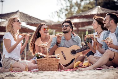 Sahilde piknik mutlu gençlerin Grup, bira içmek, yemek pizza ve birlikte eğlenmek.